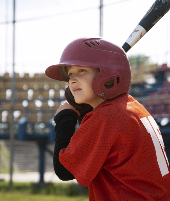 side view kid holding baseball bat wearing red baseball uniform